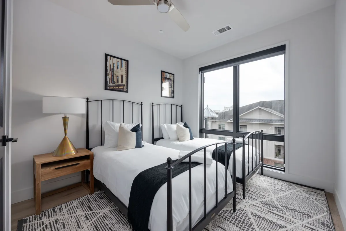 A cozy bedroom with two twin beds, decorative artwork on the walls, and a window offering a view outside. The room is bright and inviting, tailored to create a comfortable and serene space for guests to unwind together.