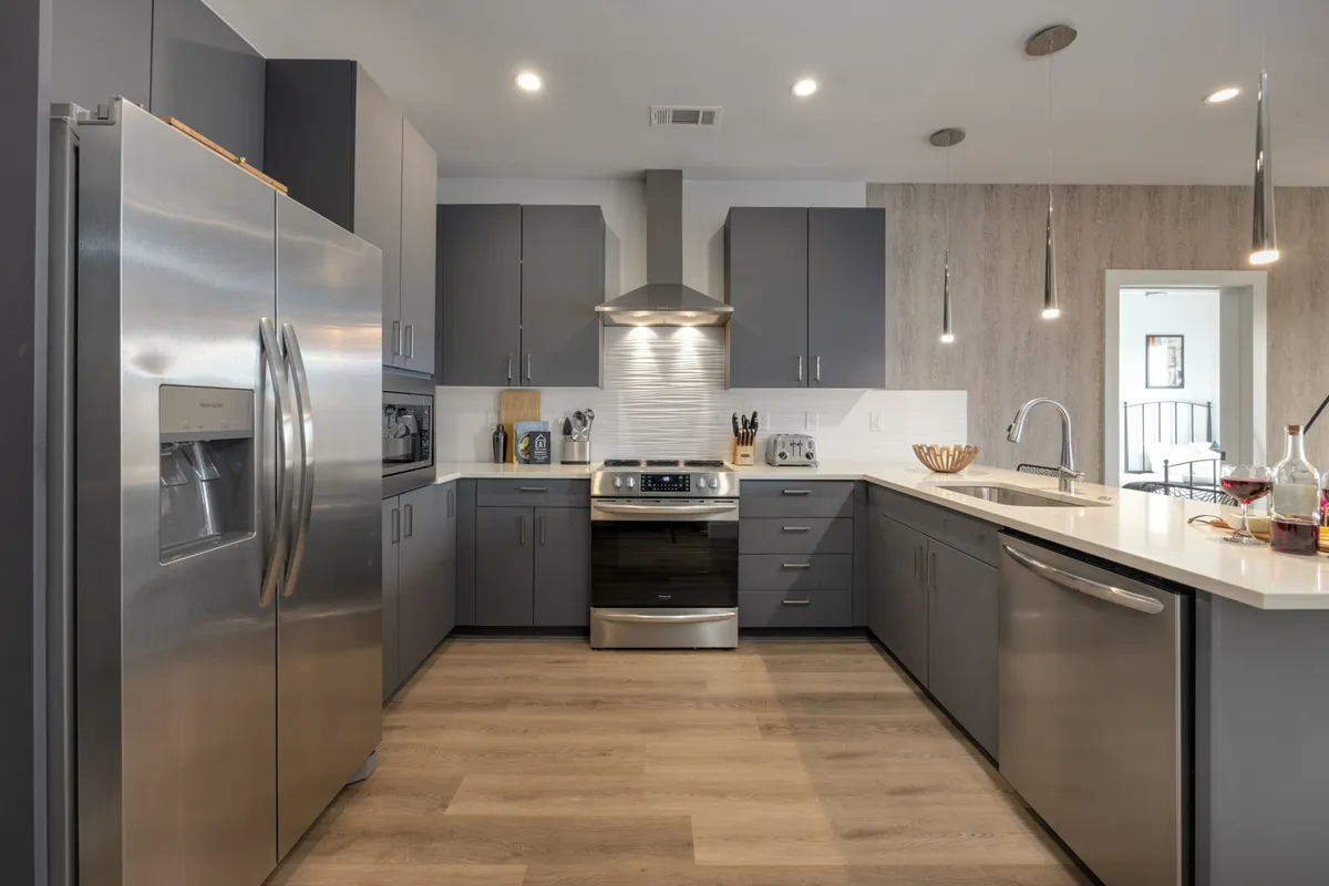 A contemporary kitchen space featuring a stainless steel refrigerator, a modern kitchen island with sleek bar stools, smooth cabinetry, and a stovetop with an overhead hood. The open layout suggests ample space for meal preparation and casual dining.