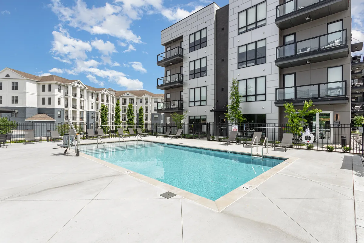 A resort-style swimming pool framed by well-maintained landscaping and building balconies, with space for swimming, sunbathing, and outdoor gatherings. The sunset lighting and community vibe reflect a relaxed, upscale atmosphere.