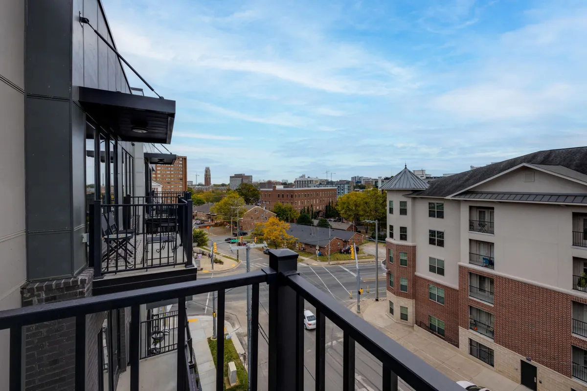 A view from a balcony captures the city skyline and neighboring buildings, with a tree-lined street below. The scene is lively and connected to the urban energy, aligning with the idea of starting the day with coffee on the balcony and being steps away from the city’s attractions.