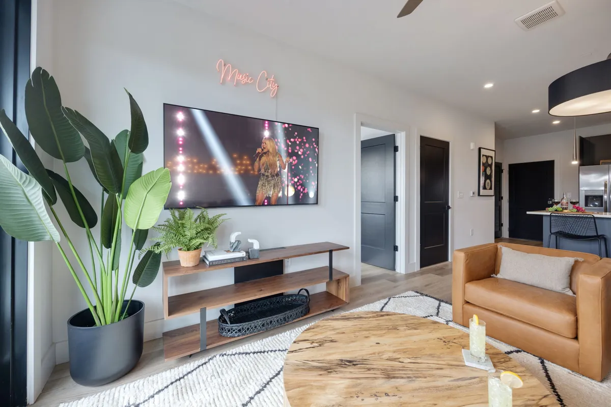 A living space featuring a large-screen smart TV, a comfortable sofa, a wooden coffee table, and a touch of greenery from a potted plant. The setup highlights an entertainment-focused area perfect for movie nights or socializing.