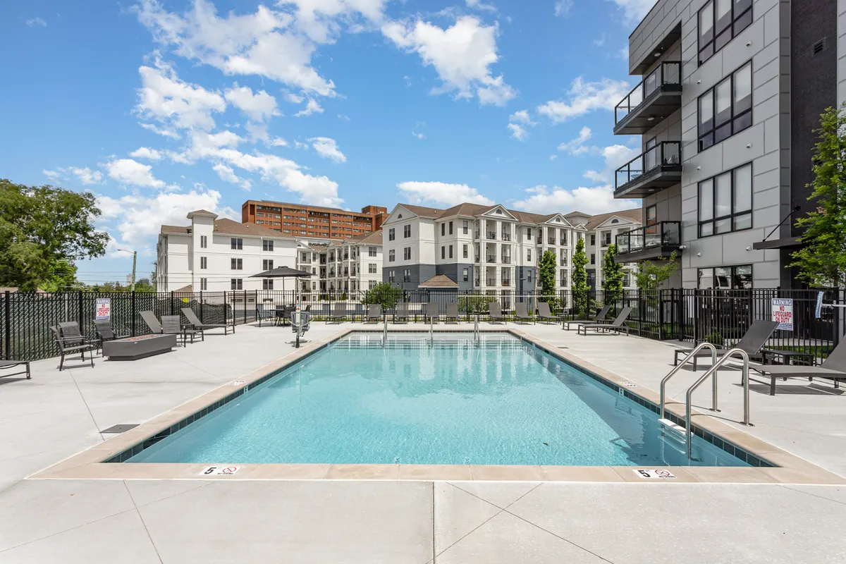 A sparkling swimming pool surrounded by lounge chairs and buildings, inviting residents to swim, sunbathe, relax, or socialize in a laid-back setting.